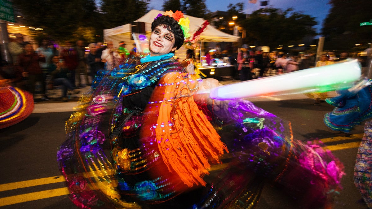 A parade participant in colorful costume walks down a street