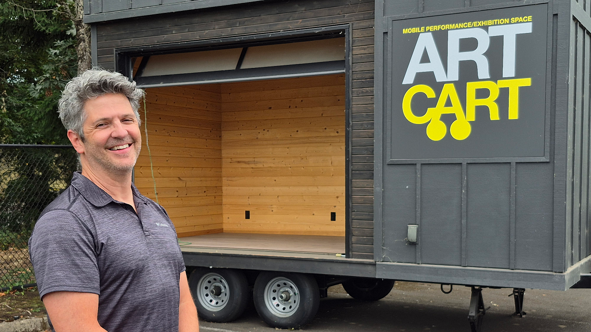A person stands in front of a mobile stage with a sign that reads Art Cart