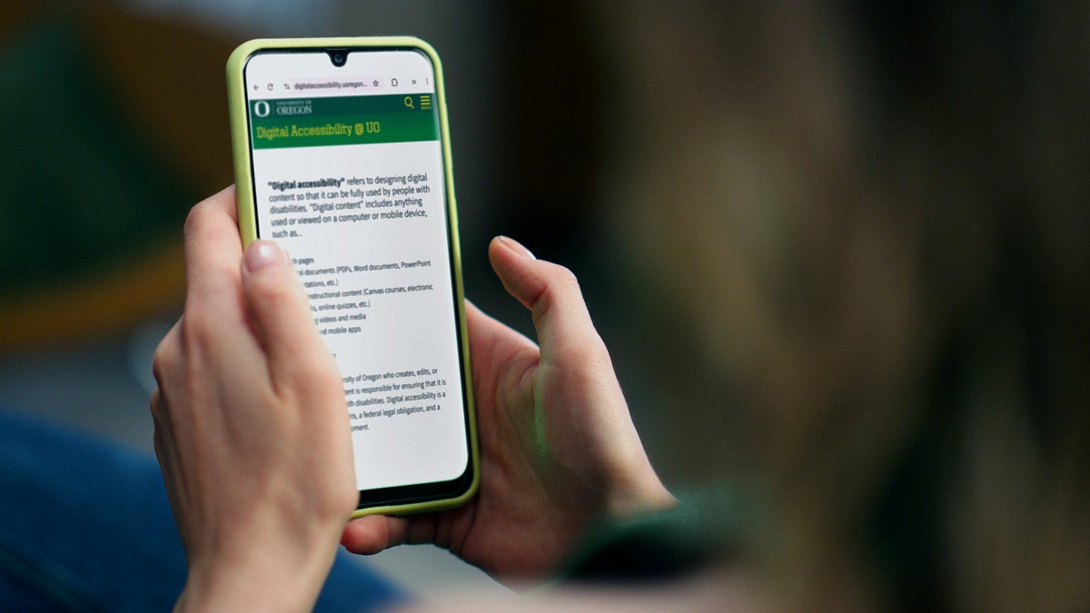 A person holds a smartphone reading a page about digital accessibility at the UO