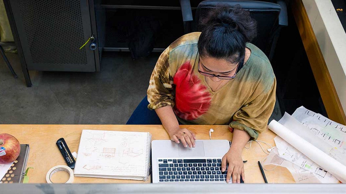 Overhead view of Dristi Manandhar working on a computer surrounded by architecture plans