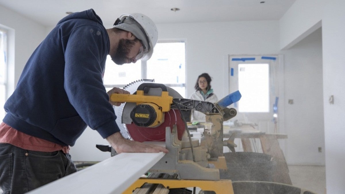 One student cuts a baseboard while aother prepares another baseboard for cutting.