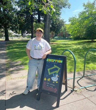 An employee stands next to an easel with a sign she designed