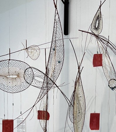 A dream catcher with images attached hangs from a gallery wall