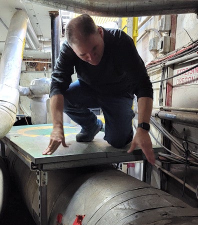A man hunches over while passing over duct work in a tight tunnel