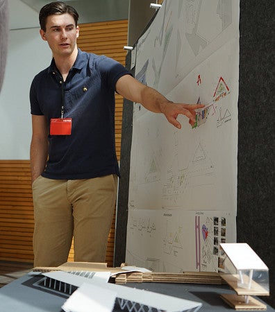 A student gestures to a wall-sized design plan for an airport