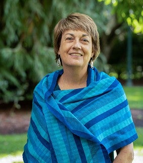 Picture of Lynn Stephen outside with green background and wearing a blue scarf