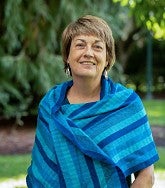 Picture of Lynn Stephen outside with green background and wearing a blue scarf