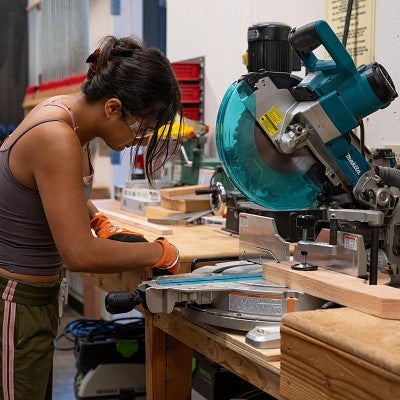 A student in a woodshop while marking on a 2-by-4 in front of a chopsaw during the Bruton Design Intensive